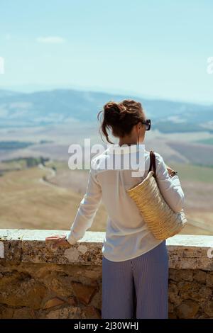 Viaggi in Italia. Vista da dietro elegante donna turistica solista con borsa di paglia a Pienza in Toscana. Foto Stock