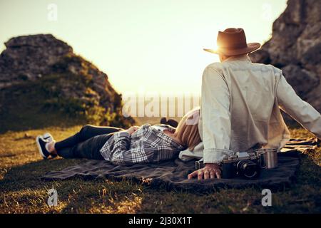 Giovane coppia che si gode un pomeriggio spensierato nella natura seduta insieme sul prato in montagna guardando il paesaggio Foto Stock