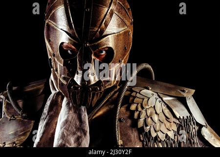 Foto di ritratto di guerriero post apocalittico in posizione eretta in maschera d'armatura e vestito su sfondo nero. Foto Stock