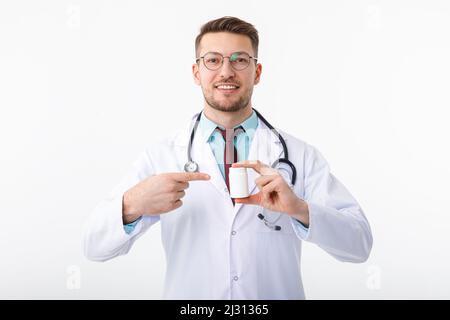 Un giovane e allegro medico maschio tiene in mano un medicinale e lo indica con un gesto. Foto Stock