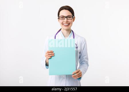 Ragazza allegra medico che tiene una cartella in mano e gesturando al copyspace. Foto Stock