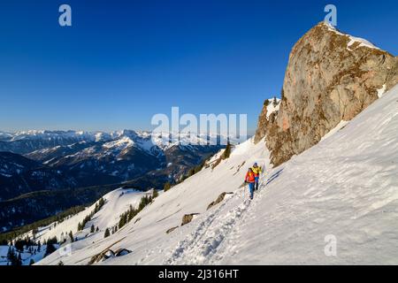 Uomo e donna che camminano fino al Rotwand attraverso il pendio di neve, torri di roccia sullo sfondo, Rotwand, Spitzing area, Alpi bavaresi, alta Baviera, Baviera, Germania Foto Stock