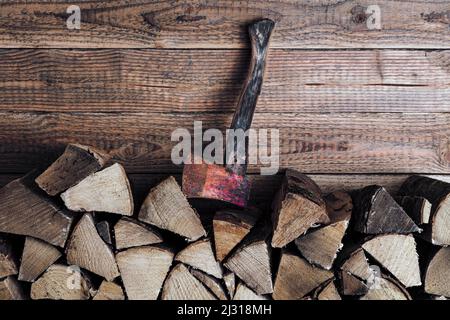 Brennholzstapel mit Axt vor Holzwand Foto Stock