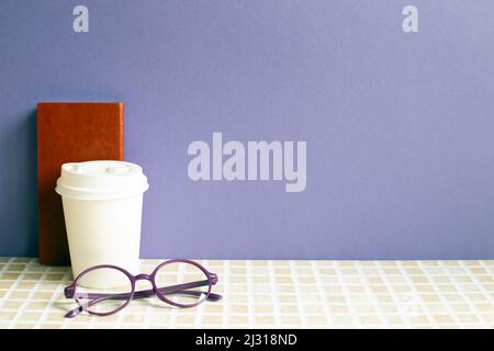 Notebook e tazza da caffè, bicchieri sulla scrivania. Sfondo viola sulle pareti. Area di lavoro Foto Stock
