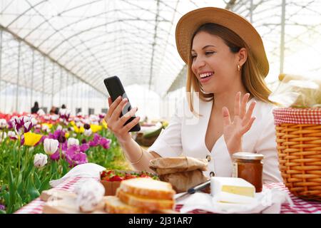 Influencer che racconta la sua esperienza con l'app mobile. Una giovane donna che videochiama con il suo ragazzo sullo smartphone mentre fa un picnic nel fine settimana Foto Stock