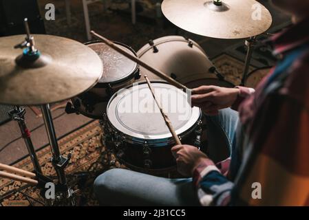 Alto angolo di raccolto anonimo musicista maschile che suona ritmo su drum set durante le prove Foto Stock