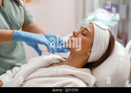 Bella giovane donna che riceve l'iniezione di acido ialuronico nel mento al salone di bellezza Foto Stock