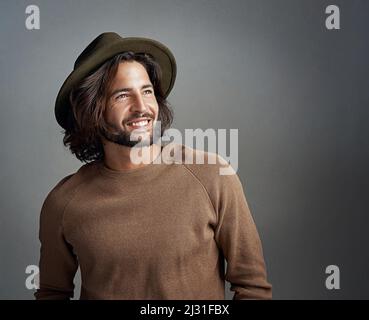 Pensare ad un nuovo cappello da aggiungere alla sua collezione. Studio girato di un felice e bel giovane uomo che indossa un cappello su uno sfondo grigio. Foto Stock