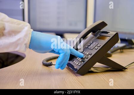 Medico in uniforme medica compone un numero di telefonoin ufficio, primo piano di una mano medica Foto Stock