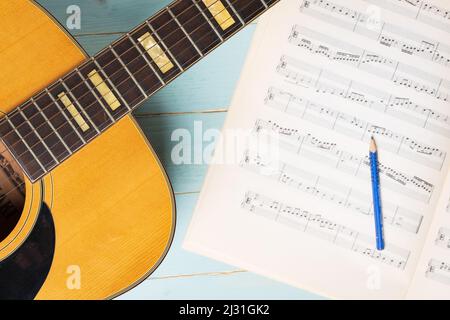 Scena di registrazione musicale con chitarra, fogli musicali e matita su tavolo di legno, primo piano Foto Stock