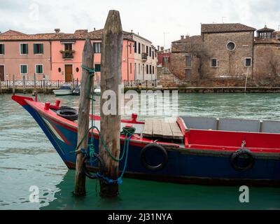 Una barca colorata è ormeggiata su uno dei canali della famosa isola di Murano, gli storici edifici colorati fiancheggiano il canale sullo sfondo, Venezia Foto Stock