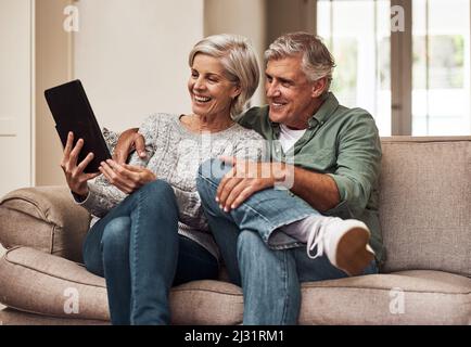 Non conosciamo più la televisione. Scatto corto di una coppia anziana allegra che naviga insieme su un tablet digitale mentre è seduto su un divano a. Foto Stock