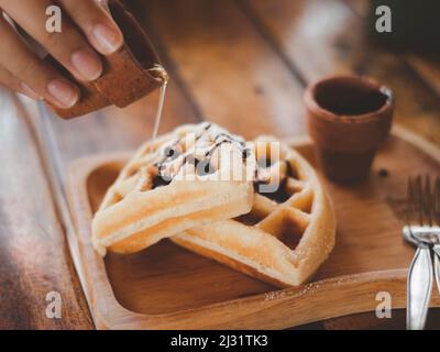 Le persone versano il miele da una caraffa bianca sul wafer, servito con una crema vergine su un vassoio rotondo, waffle Foto Stock