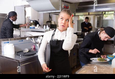 Cameriera infelice che aspetta i piatti in cucina Foto Stock