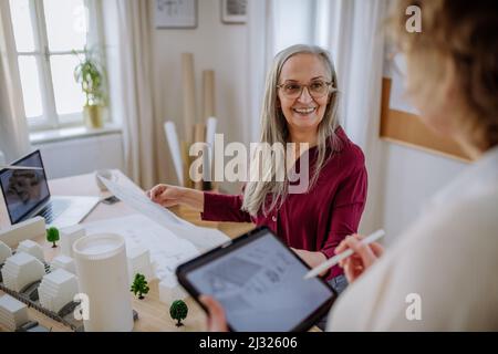 Donne mature eco architetti con progetti che lavorano su tablet insieme in ufficio. Foto Stock