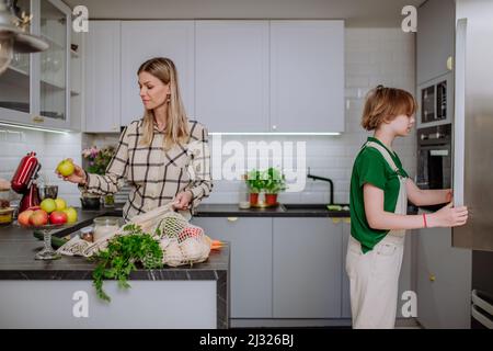 Madre disimballaggio cibo locale in confezione zero rifiuti da sacchetto con l'aiuto di figlia in cucina a casa. Foto Stock