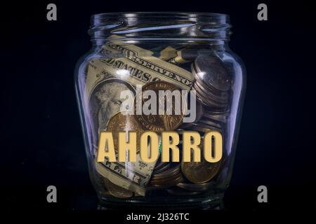 Vaso pieno di monete e dollaro fattura AHORRO testo sfondo nero Foto Stock