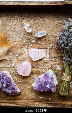 Sopra la vista di due cristalli di quarzo rosa lucido di colore rosa su vassoio di legno in casa. Attrarre l'amore, cuore che guarisce chakra concetto. Bouquet di lavanda secca Foto Stock