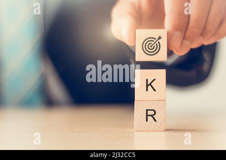Business plan con OKR (obiettivi e risultati chiave). L'uomo tiene blocchi di cubo di legno con icona di obiettivo e testo OKR. Per lo sviluppo delle prestazioni aziendali. CA Foto Stock