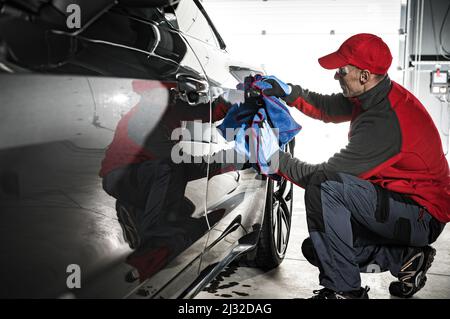 Professionale Automotive Worker pulizia carrozzeria auto con panno morbido subito dopo il processo di lavaggio a pressione. Tema dell'industria dei trasporti. Foto Stock