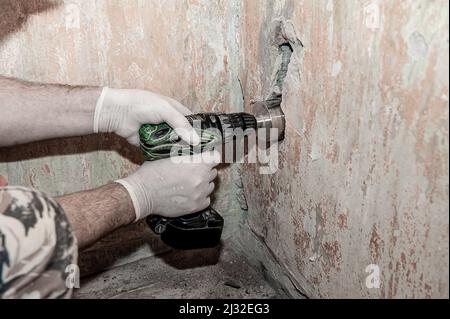 Close-up. Le mani del lavoratore, protette da guanti, stanno perforando una parete di calcestruzzo con un trapano elettrico. Vita reale, riparazioni fai-da-te. Spazio copia . Foto Stock