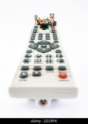 La famiglia passa il tempo insieme a navigare sul canale e guardare una televisione, fotografia concettuale. Figurine in miniatura sul telecomando della TV, guardando la partita Foto Stock