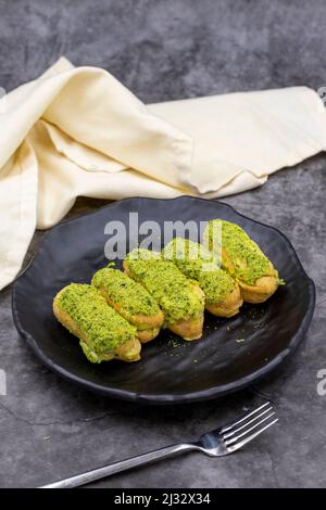 Torta di eclair al pistacchio su sfondo scuro. Prelibatezze della cucina internazionale. Primo piano Foto Stock