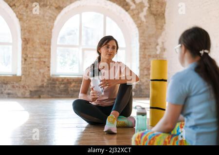 Giovane donna con sindrome di Down che parla con il suo allenatore yoga al chiuso Foto Stock