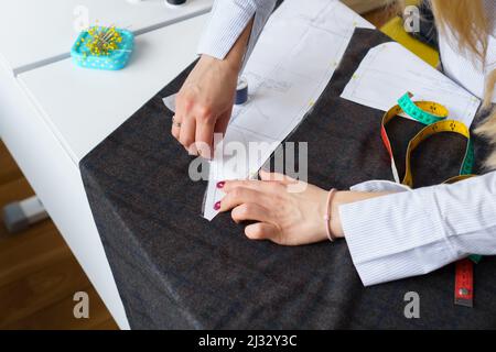 Il dressmaker contrassegna un pezzo di tessuto con gesso in base al modello di carta. Lavoro di sarto, utensili per cucire Foto Stock