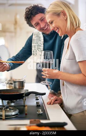 Tutto ha un gusto migliore quando sei innamorato. Shot di una felice coppia che cucinano la cena insieme nella loro cucina. Foto Stock