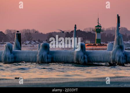 Vecchio molo di legno ghiacciato sulla spiaggia all'alba, sullo sfondo luce del molo (faro), Travemünde, Baia di Lübeck, Schleswig Holstein, Germania Foto Stock