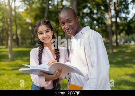 Concetto di istruzione. Studenti universitari amichevoli multirazziali che si preparano per l'esame insieme, tenendo notebook e sorridendo Foto Stock
