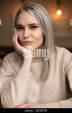 Ritratto di giovane attraente donna seria con lunghi capelli grigi con riccio professionale poggiante mento a portata di mano. Foto Stock