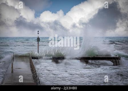 Onde dell'oceano tempestose che si infrangono su un molo durante una tempesta degli inverni Foto Stock