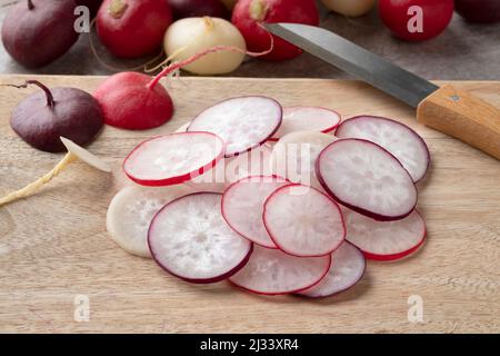 Un mucchio di rafano fresco rosso, bianco e viola affettato da vicino su un tagliere Foto Stock