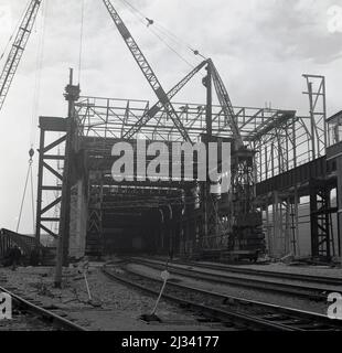 1950s, grandi gru storiche e un enorme portale che copre i binari ferroviari presso l'impianto di acciaio Abbey Works, Port Talbot, Galles, Regno Unito. I Gantries sono utilizzati in grandi luoghi industriali per il carico di materiali pesanti alla rinfusa. Foto Stock