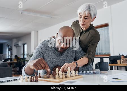 Niente può interrompere la sua attenzione. Colpo di un uomo d'affari maturo che ottiene l'aiuto da un collega mentre gioca a scacchi nel suo ufficio. Foto Stock