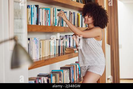 Alberi tatuati per un mondo in un raccoglitore. Scatto di una giovane donna attraente che naviga in una mensola del libro a casa. Foto Stock