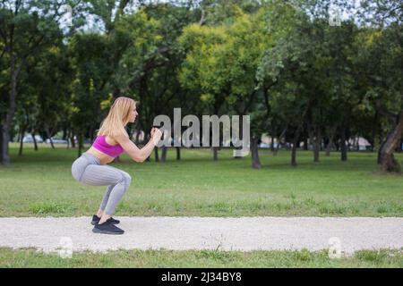 adatta la giovane donna che fa squat nel parco Foto Stock