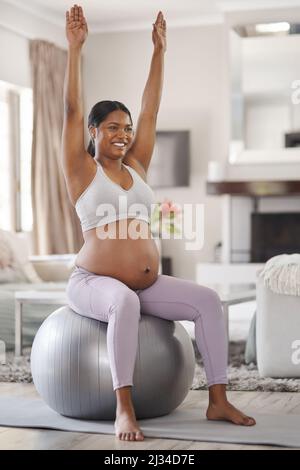 Stretching sicuro aiuta con dolori e dolori di gravidanza. Scatto di una bella giovane donna incinta che si esercita a casa. Foto Stock