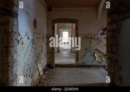 Corridoio scuro in un edificio pubblico abbandonato accanto alla scala. Esplorazione urbana in una vecchia casa horror. La vernice si stacca dalle pareti sporche. Foto Stock