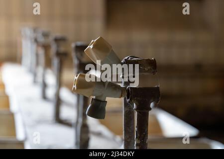 Vecchio rubinetto dell'acqua rotto con ruggine sui tubi. Maniglia in plastica davanti a una fila di lavelli. Primo piano dell'attrezzatura in un edificio abbandonato. Foto Stock