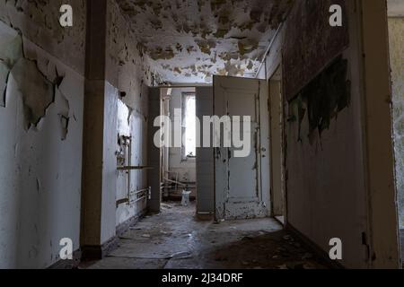 Corridoio scuro in un edificio pubblico abbandonato con una porta aperta creepy. Esplorazione urbana in una vecchia casa horror. La vernice si stacca dalle pareti. Foto Stock