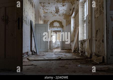 Corridoio lungo e scuro in un edificio pubblico abbandonato con molte porte di legno. Esplorazione urbana in una grande vecchia casa. La vernice si stacca. Foto Stock