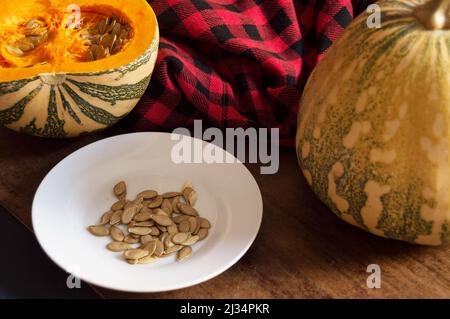 Piatto con semi di zucca e un'altra zucca dimezzata e una intera accanto ad un panno rosso a scacchi Foto Stock