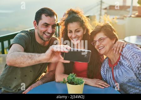 Voglio ricordare questo giorno per sempre. Scatto corto di una famiglia affettuosa di tre che prende selfie mentre si siede fuori. Foto Stock