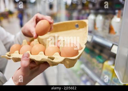 Mano di un cliente che tiene un cartone di uova fresche biologiche mentre acquista al supermercato Foto Stock