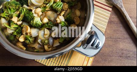 Immagine realizzata da sopra di una padella con broccoli saltati, funghi, aglio affettato e cipolle tritate grossolanamente, la padella si trova su un piccolo bambù m Foto Stock