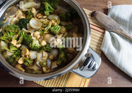 Vista dall'alto della padella con broccoli saltati, funghi, aglio a fette e cipolle tritate grossolanamente Foto Stock