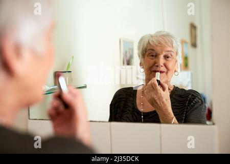 Non hai mai avuto l'età di giocare il femme fatale. Ritratto di una donna anziana felice che applica il trucco mentre osserva nello specchio. Foto Stock